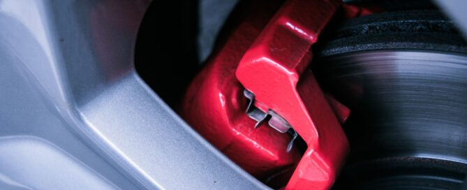 Red brake caliper and brake rotor behind a car wheel
