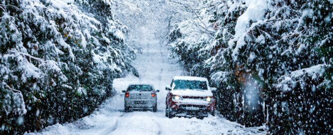 Two cars on a snow-covered tree-lined road during a winter snowfall